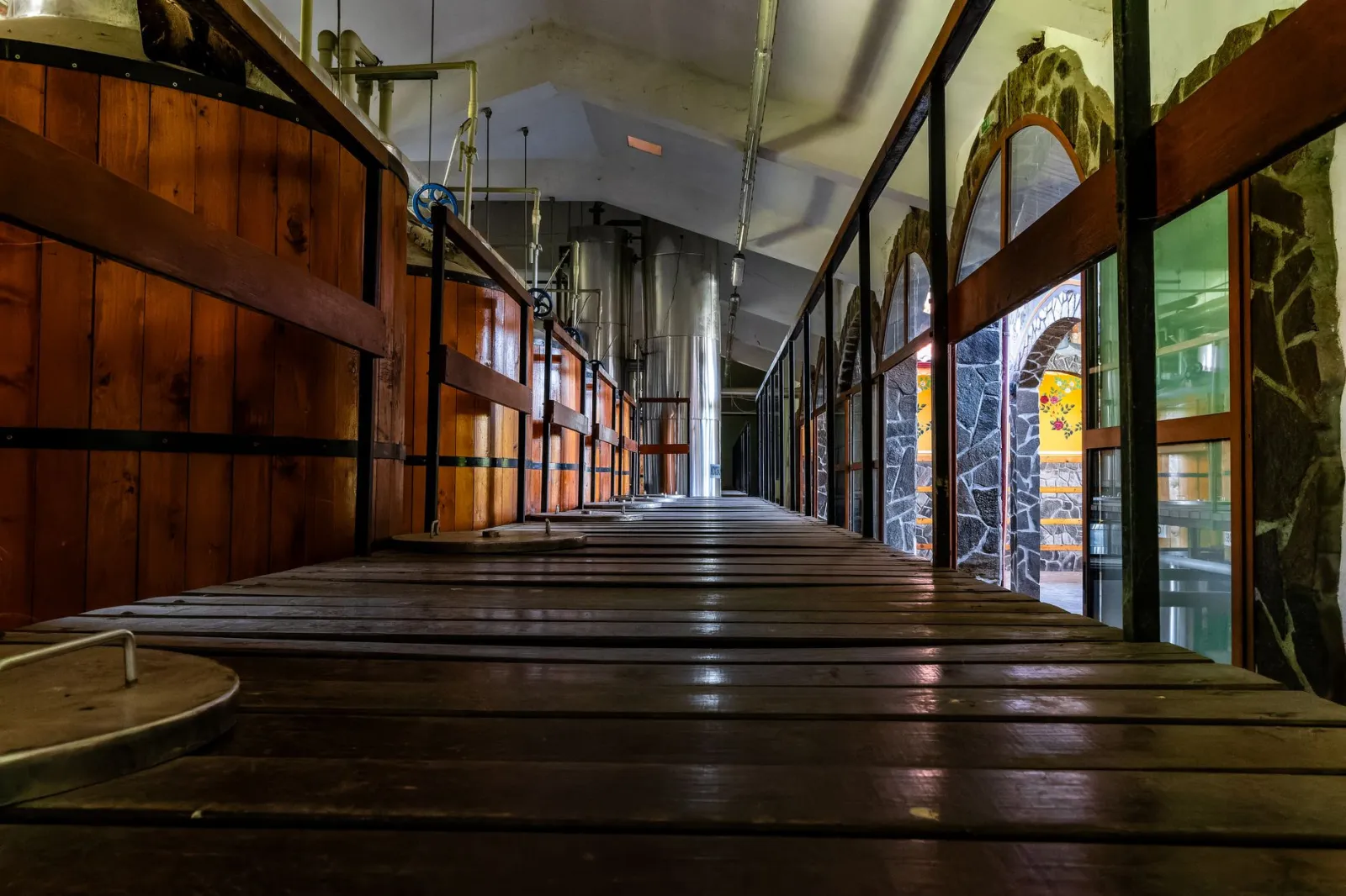 Wide-angle view of a rustic brewery interior showcasing wooden fermentation tanks and industrial brewing equipment.