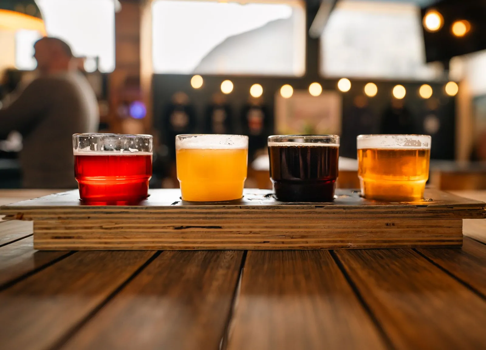 Flight piw na drewnianym stole w kameralnym taproomie, para degustująca piwa