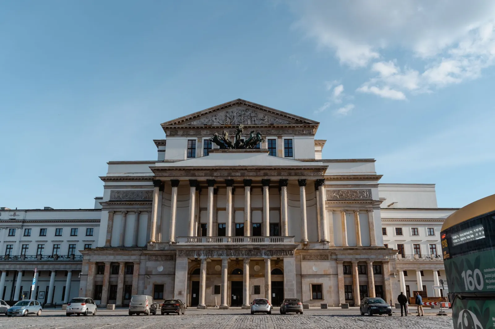 Zadbana fasada miejskiego teatru z ludźmi podchodzącymi do wejścia.