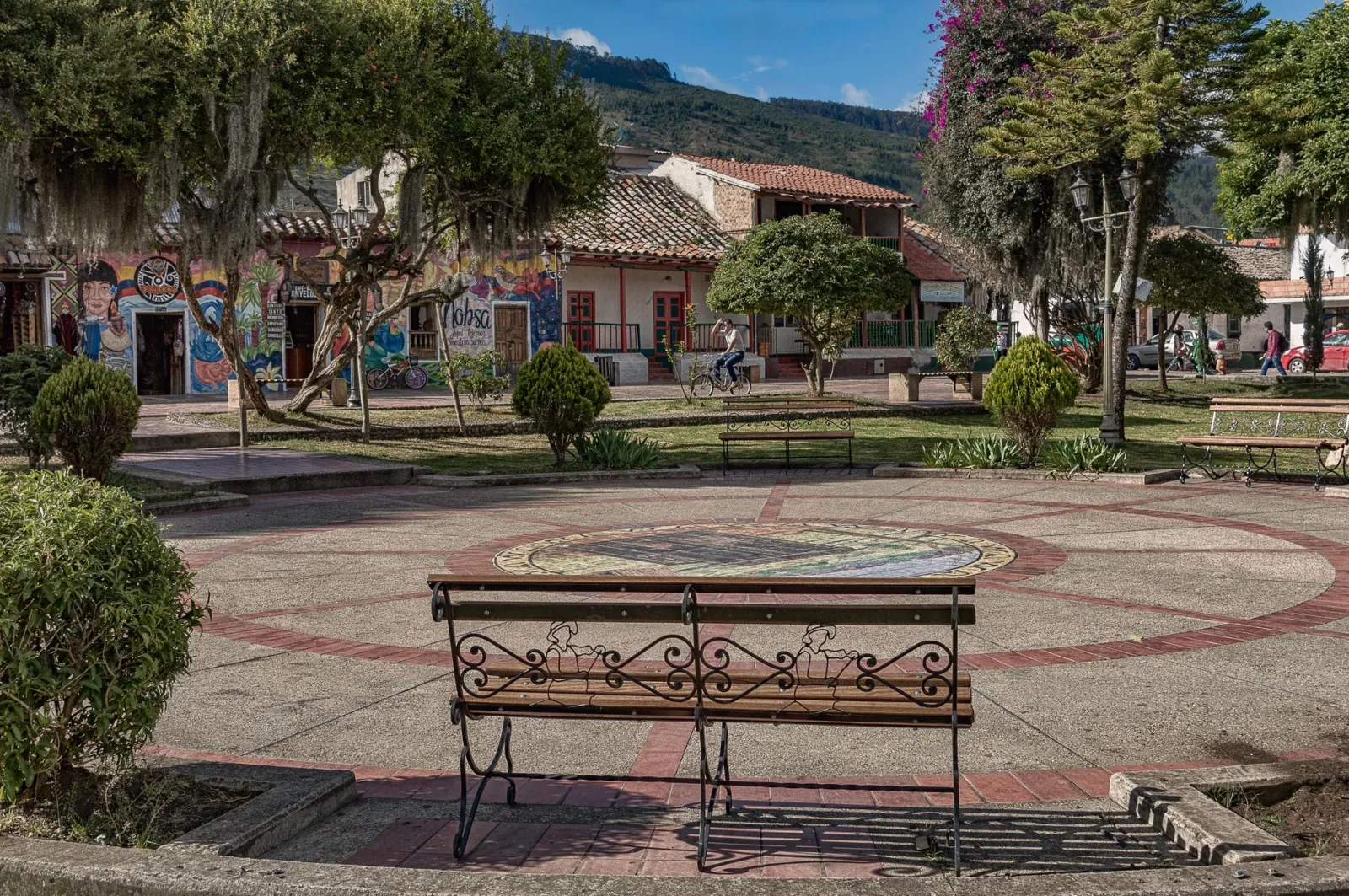 Peaceful town square with benches, art murals, trees, and historic buildings on a sunny day.