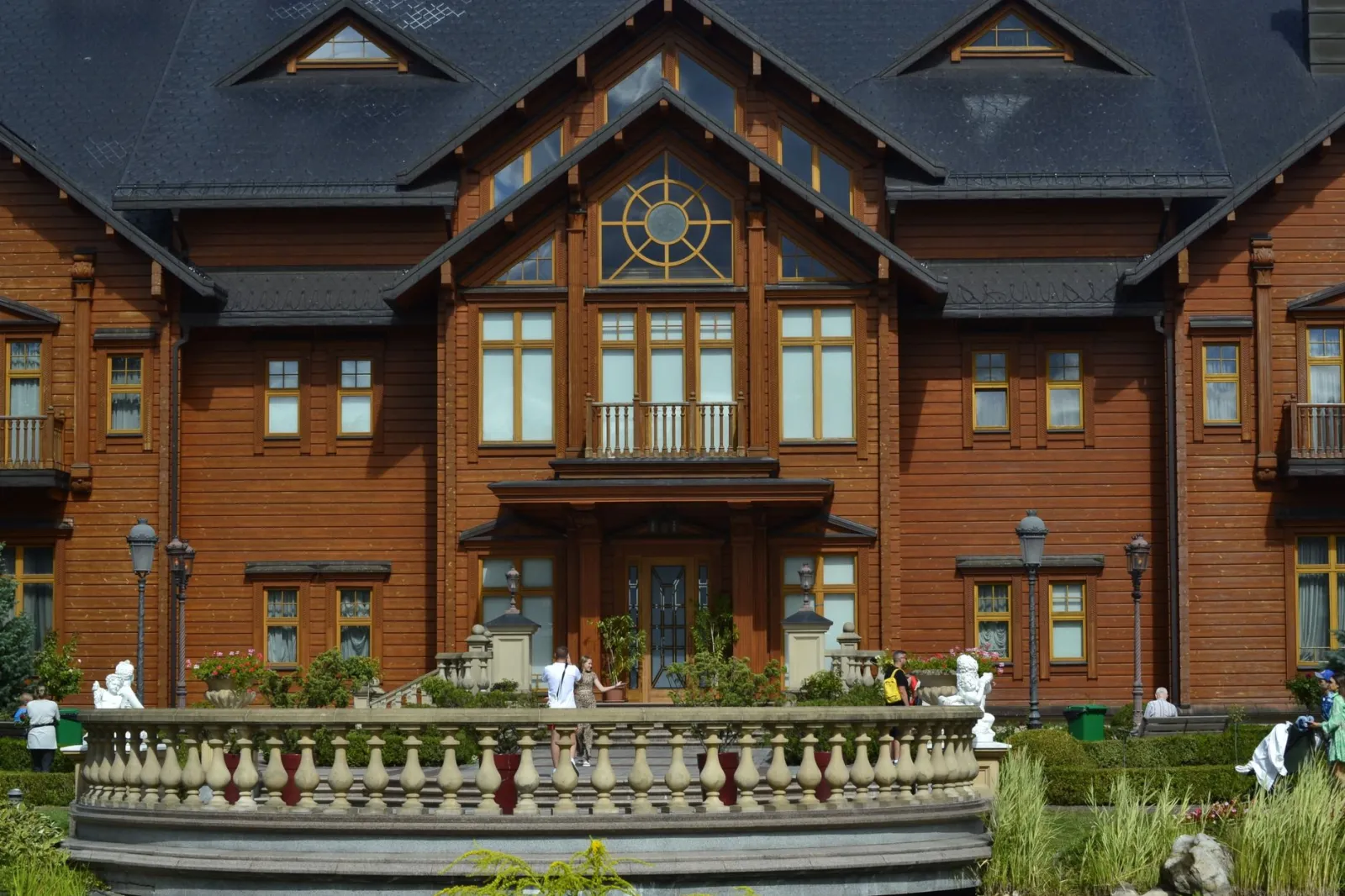 Taras z balustradą i rzeźbą, geometryczne rabaty i alejki ogrodu w tle.