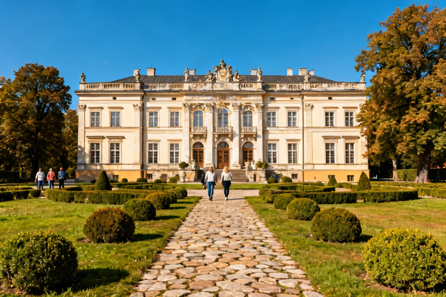Elewacja barokowego pałacu z zadbanym dziedzińcem i przechodniami