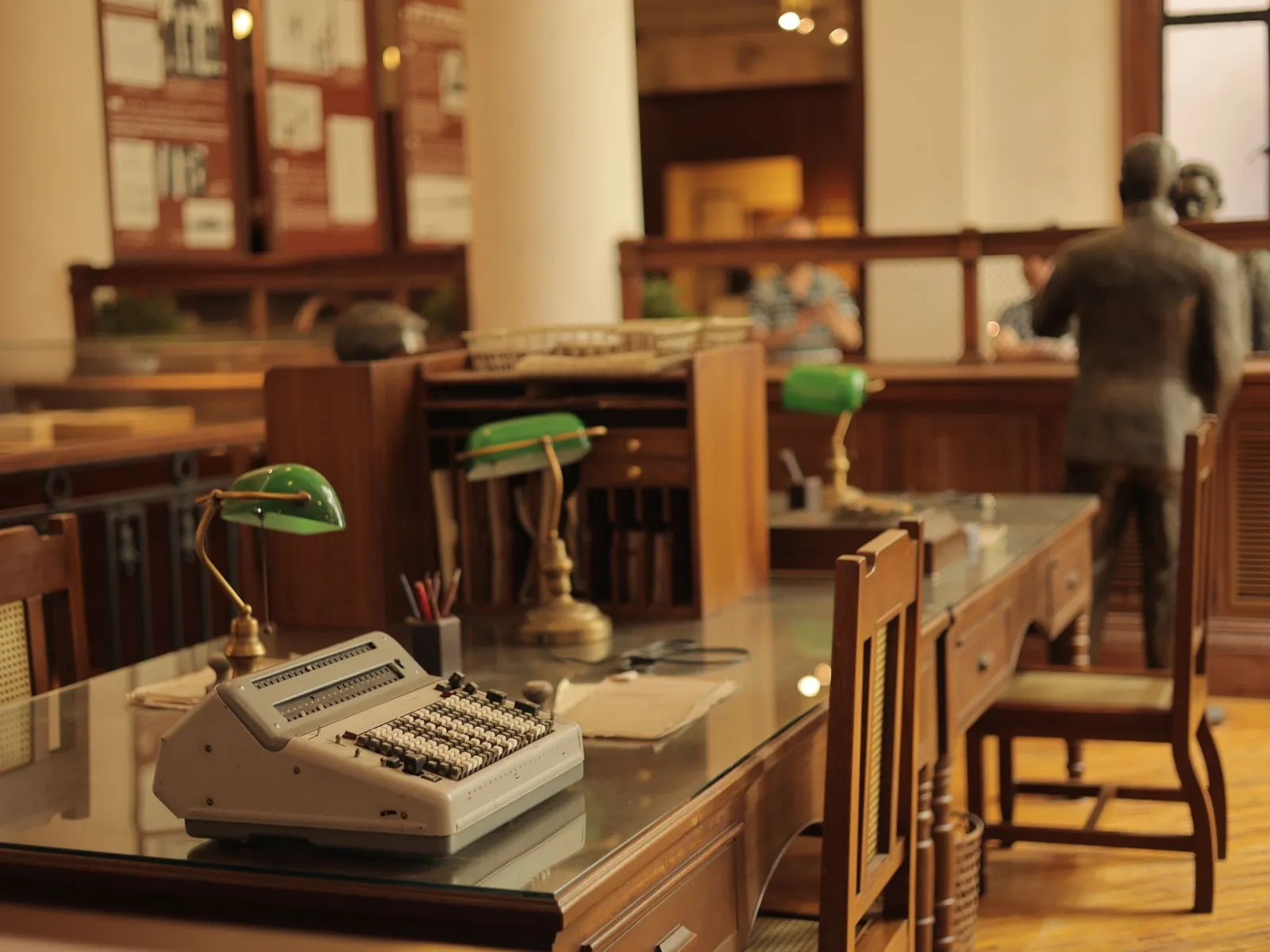 A classic office interior featuring a vintage typewriter, green desk lamps, and wooden furniture.